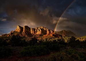 Залитые солнцем скалы после дождя с сияющей радугой